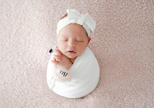 Sleeping Newborn Baby Wrapped In Swaddle Is A Studio Photo Of A Little Girl