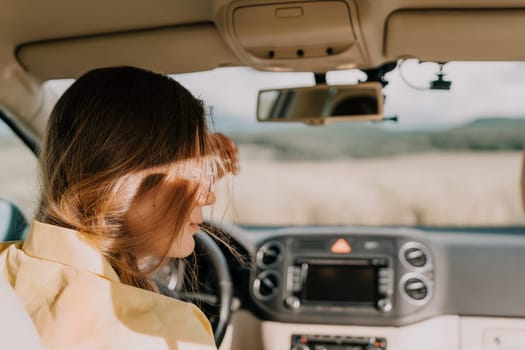 A young woman driving a car with her long brown hair blowing in the wind on a sunny day.