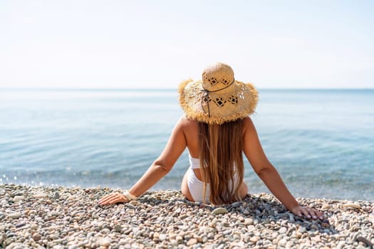 Beach Relaxation woman in hat sits on a pebble beach enjoying the sunshine. The concept of travel, vacation at sea.