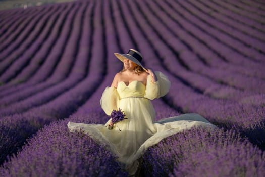 Woman poses in lavender field at sunset. Happy woman in yellow dress holds lavender bouquet. Aromatherapy concept, lavender oil, photo session in lavender.