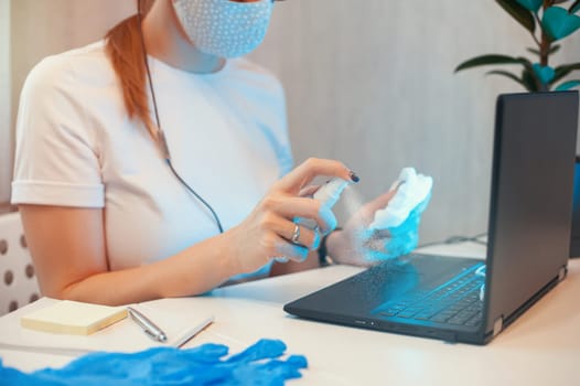 Woman disinfects the surface of the phone by sanitizer spray on the working place. Coronavirus concept. Woman in quarantine for coronavirus covid-19 working from home.