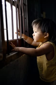 Little boy standing behind the window in sad mood.