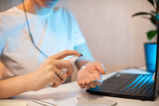 Woman disinfects the surface of the phone by sanitizer spray on the working place. Coronavirus concept. Woman in quarantine for coronavirus covid-19 working from home.