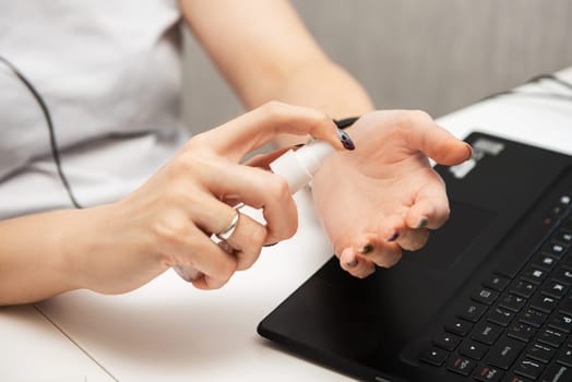 Woman disinfects the surface of the phone by sanitizer spray on the working place. Coronavirus concept.