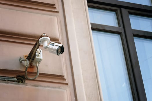 A contemporary surveillance camera is securely mounted next to the window on the exterior of a building, promoting safety and security to minimize robbery