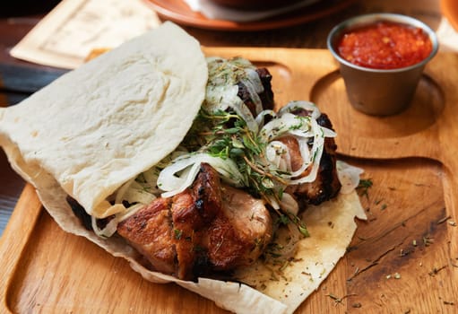 Appetising kebab with onions wrapped in lavash on a wooden tray