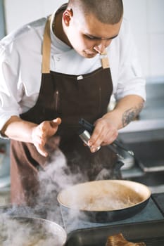 Young attractive male cook with uniform preparing a meat sause. The figure in a bent form.