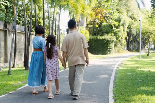 A family of three walking along a paved path in a lush, green park, enjoying a sunny day and spending quality time together.