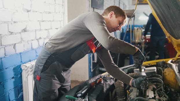 Mechanic in car repairing service - diagnostics in engine compartment, close up