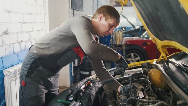 Mechanic in car repairing service - diagnostics in engine compartment, close up