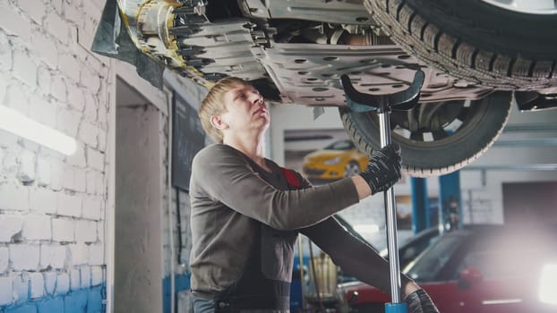 Mechanic unscrewing parts of automobile's bottom under lifted car, close up