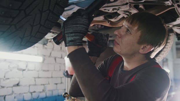 Mechanic with thr lamp is checking the bottom of car in garage automobile service, close up view
