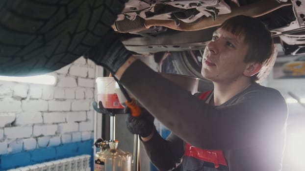 Mechanic with thr lamp is checking the bottom of car in garage automobile service, close up, telephoto