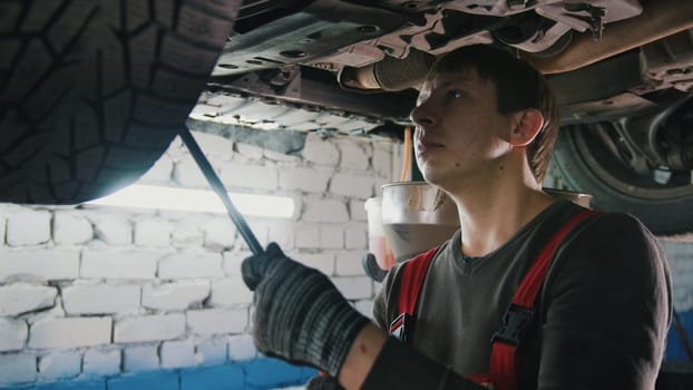 Mechanic with thr lamp is checking the bottom of car in garage automobile service, close up, telephoto