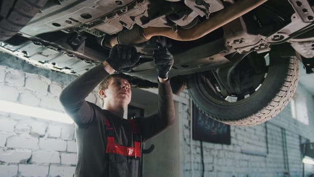 Mechanic with the wrench is repairing bottom of the car in garage automobile service, close up view