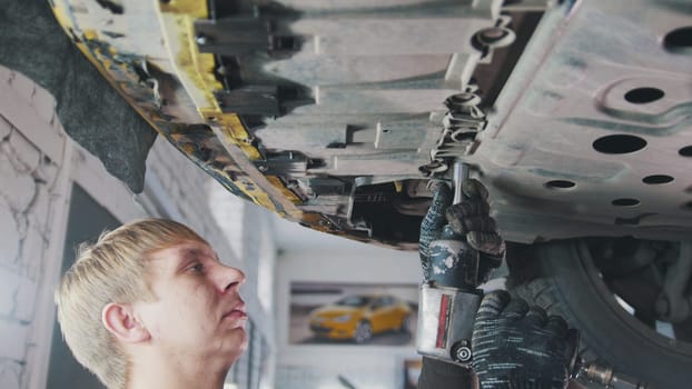 Car auto service - mechanic unscrews detail of car under bottom of vehicle, close up