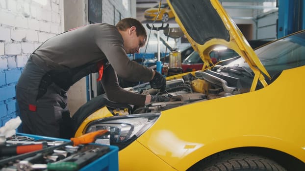 Mechanic unscrews detail near yellow car - automobile service repairing, close up view