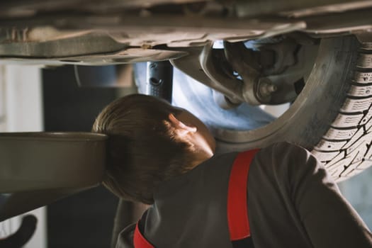 Mechanic unscrewing parts of automobile's bottom under lifted car, close up