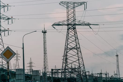 A low angle view of power lines and towers against a cloudy sky with a street lamp in the foreground.