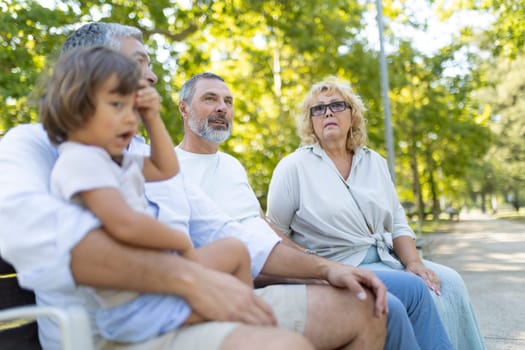 Multi-generational family is spending quality time together, sitting on a bench in a park