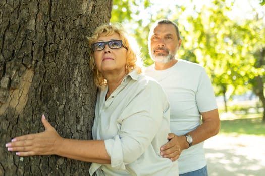 Retired couple holding each other and hugging a tree in the park on a sunny day