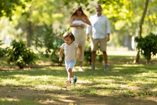 Young boy running ahead of his family while enjoying a sunny day at the park