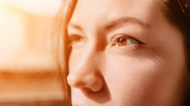 A close-up shot of a woman's eye with brown iris and dark eyeliner, in warm sunlight.