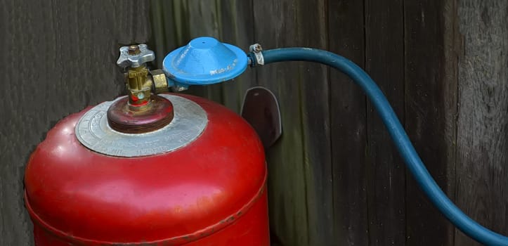 Close-up of a red gas cylinder with a blue regulator and hose connection on a wooden background, concept of energy and safety