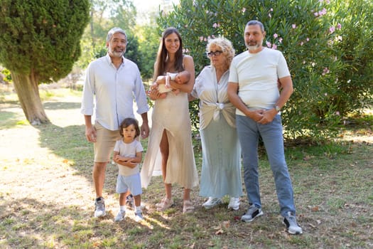Family is posing in the park with their newborn baby, enjoying the sunshine and fresh air