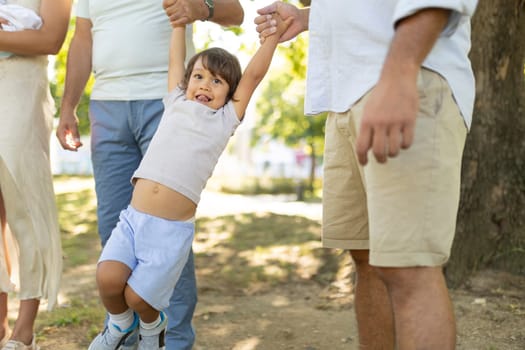 Happy family is enjoying a sunny day at the park, swinging their young son through the air