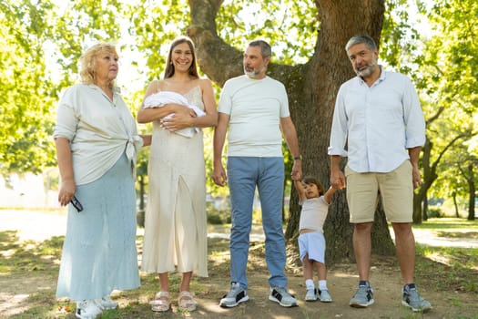 Family is gathering in a park, celebrating the arrival of a newborn baby