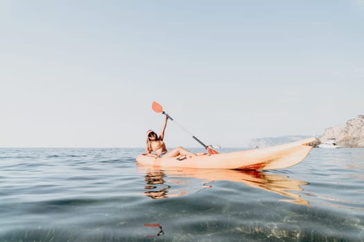 A person paddles a yellow kayak on calm blue water with a mountain in the distance.