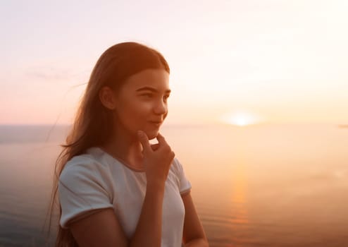 A young girl with long brown hair stands by a lake at sunset, lost in thought, gazing at the horizon.