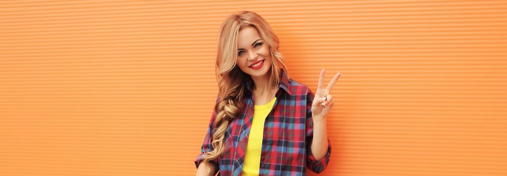 Beautiful happy smiling young blonde woman posing in casual clothes on colorful orange background in the city