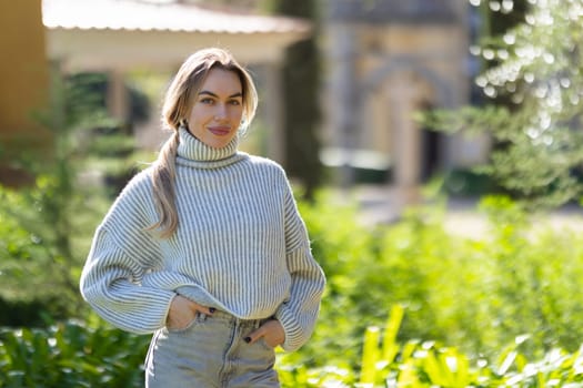 Beautiful woman posing in green garden wearing sweater and jeans
