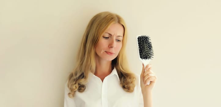 Unhappy disappointed young woman with hair loss condition, showing hair brush, blonde caucasian girl with unhealthy hair standing on white background