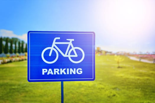 A blue rectangle traffic sign with a bicycle wheel symbol and the word parking in a skyblue font, set against a natural landscape backdrop