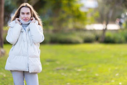 Young woman is bundling up in her warm winter clothes on a sunny but cold day in the park