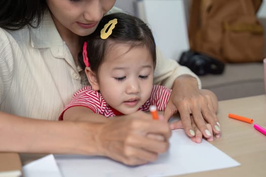 A mother lovingly guides her young daughter as they draw together, highlighting the bond and creativity in a cozy home setting.