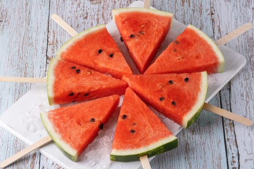 Fresh watermelon slices on sticks with ice.