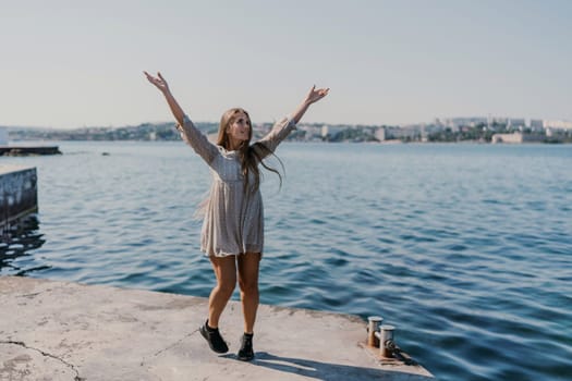 A woman is standing on a dock by the water, wearing a dress and a pair of black shoes. She is smiling and she is happy