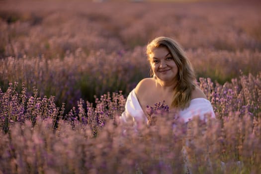 Woman poses in lavender field at sunset. Happy woman in white dress holds lavender bouquet. Aromatherapy concept, lavender oil, photo session in lavender.