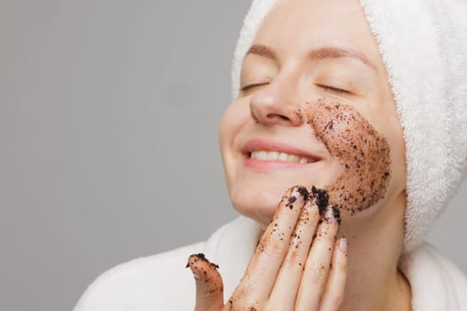 Woman enjoying facial skin care, applying black coffee face scrub, concept of rejuvenation and facial skin care