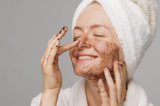 Woman enjoying facial skin care, applying black coffee face scrub, concept of rejuvenation and facial skin care