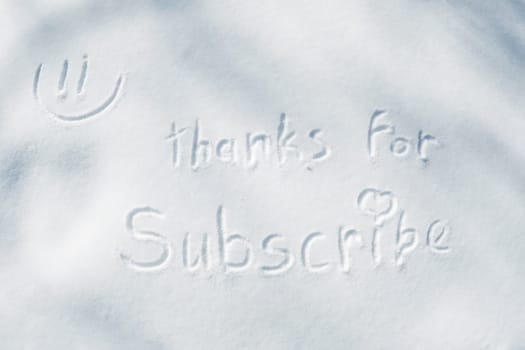 The inscription THANKS FOR SUBSCRIBE with a heart and a smiley face, written with a finger on the snow.