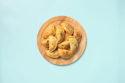 Top view baked samsa pies with chicken sprinkled with poppy seeds on wooden plate on blue background.