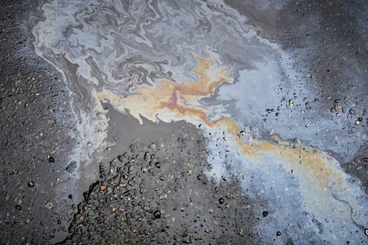 A close-up of a shiny fuel spill on wet pavement, shot from above