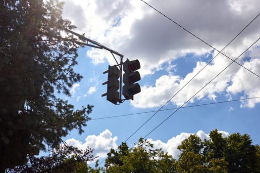 Traffic lights on the background of a bright sunny sky with clouds in the city. Framed by trees.
