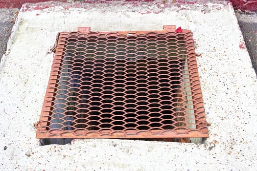 an old steel grating hatch on a concrete curb. Cement base.