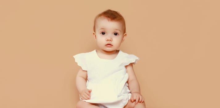 Portrait of happy cute baby sitting on the floor looking at camera on brown studio background